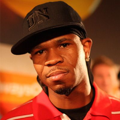 A rapper in a black snapback hat and a red shirt.