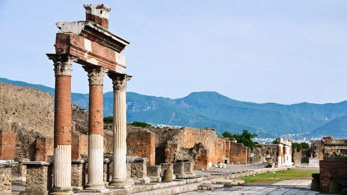 Ancient ruins in Pompeii Archaeological Park. Ancient ruins with columns at Pompeii Archaeological Park, with mountains in the background.