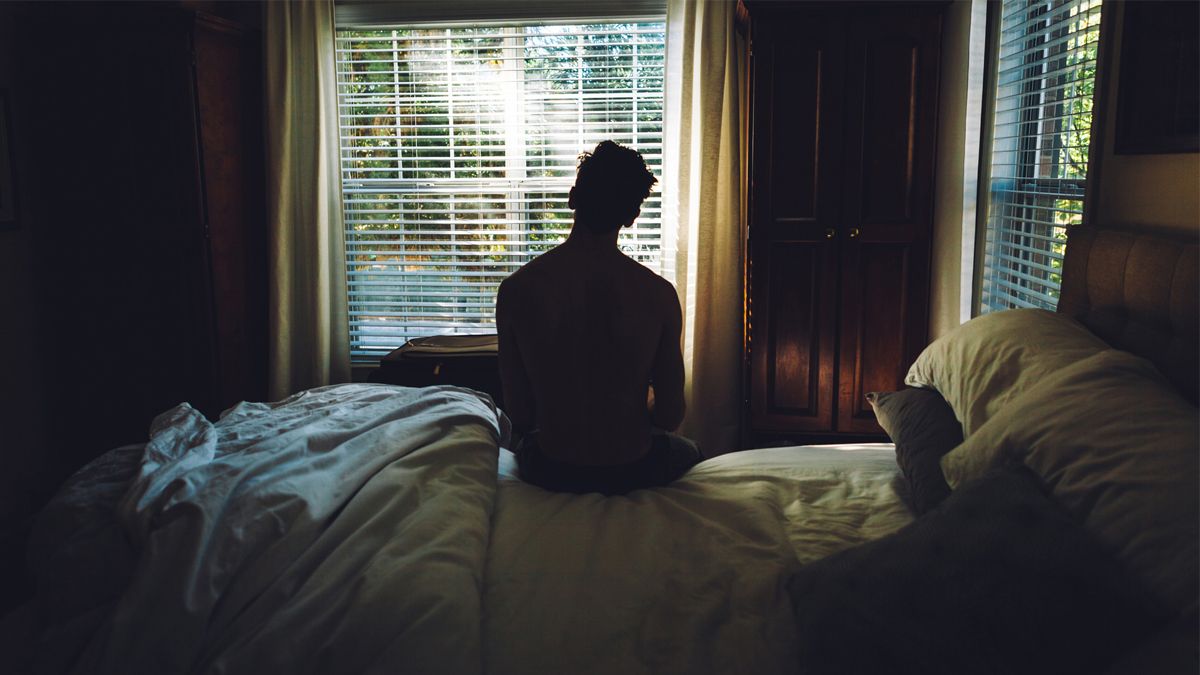 A man sat alone in the dark on his bed suffering from depression and anxiety,