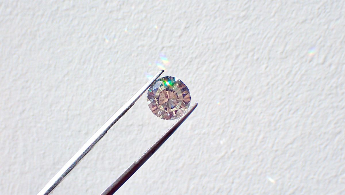 A diamond held with tweezers against a white wall.