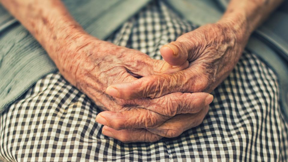 An elderly person's hands rest in their lap.