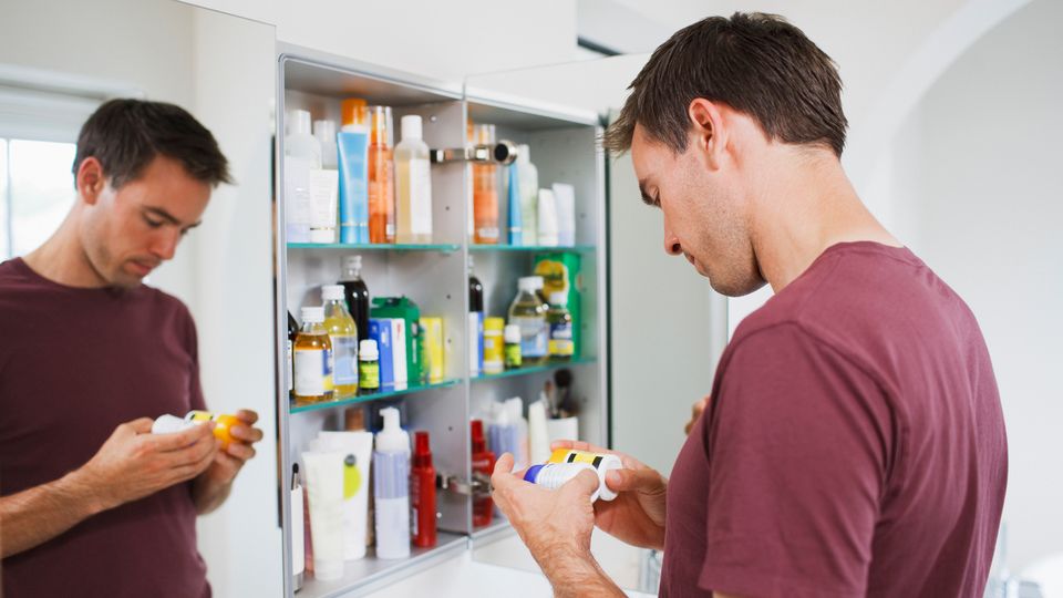 A man examining pill bottles in front of bathroom cabinet, illustrating male contraceptive pill use.