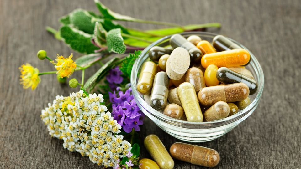 A bowl containing herbal medicines next to various herbs.