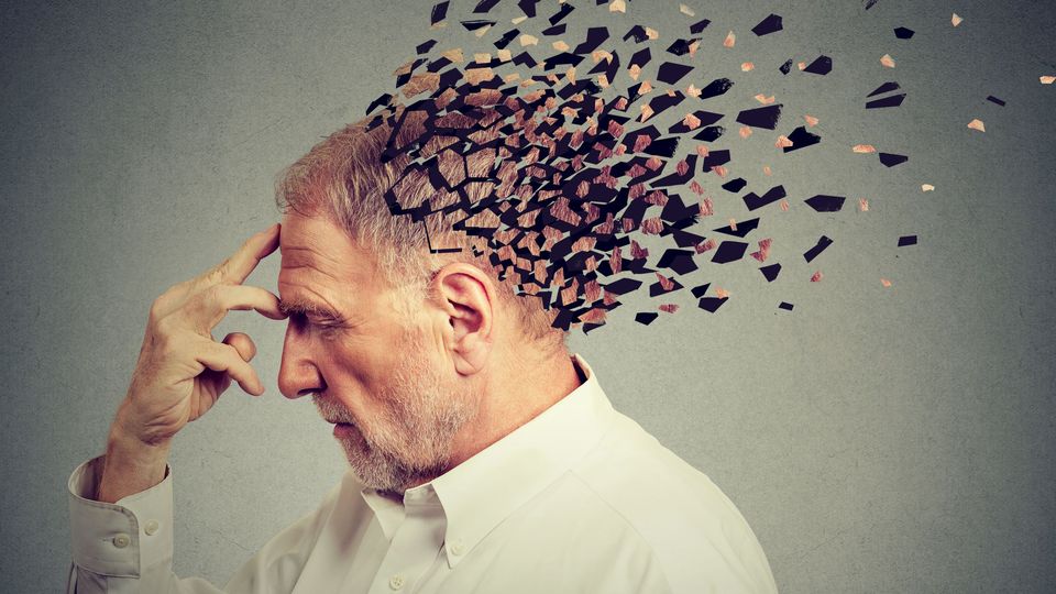 An older man holding his head, which is breaking into pieces, representing cognitive decline in dementia patients.