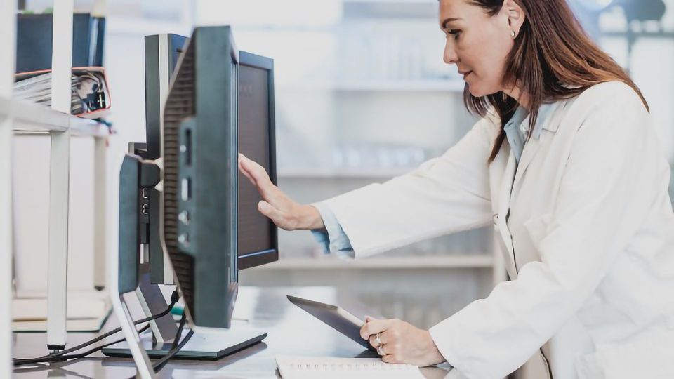 A researcher in a lab coat touches a computer screen.