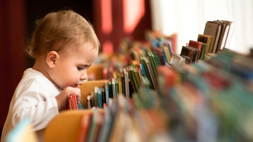 A baby looking through books. 