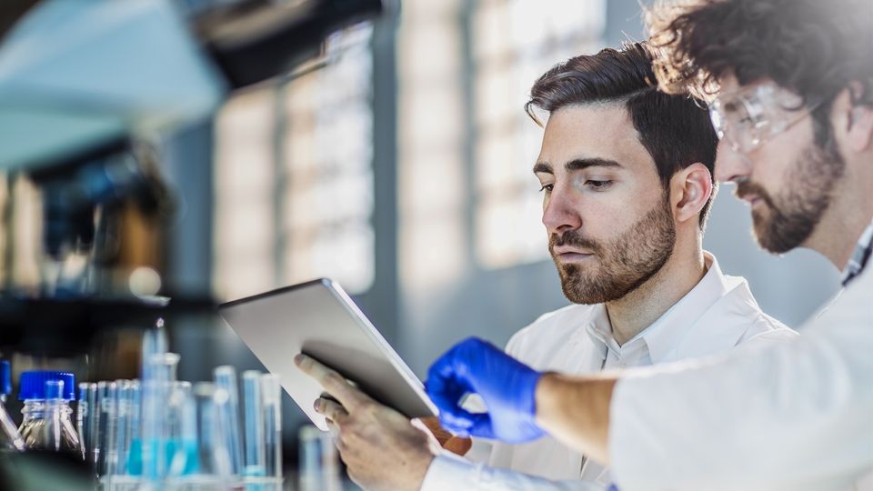 Two male scientists look at a tablet.