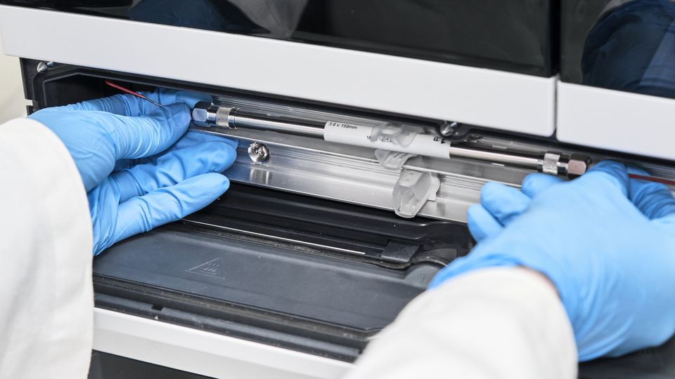A scientist places a tube into a chromatography machine.