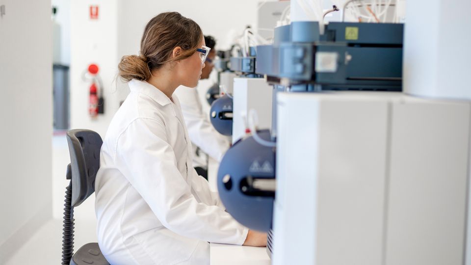 A scientist in a lab coat sits at a machine.