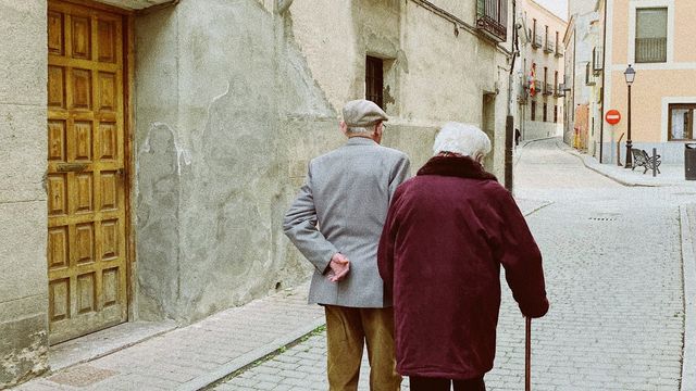 Two elderly people walk side by side down a street.  