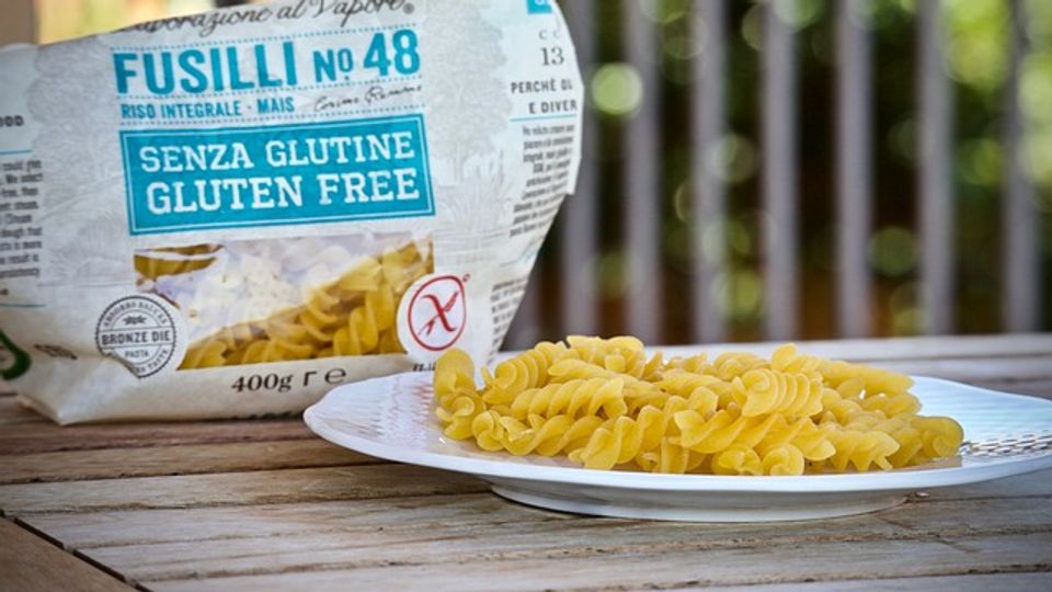 Some gluten free pasta on a plate next to a half empty pasta packet on a wooden table.