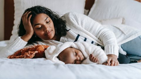 A mother lies next to her sleeping baby.