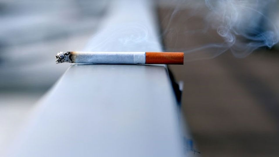 A still-smoking cigarette on a railing.