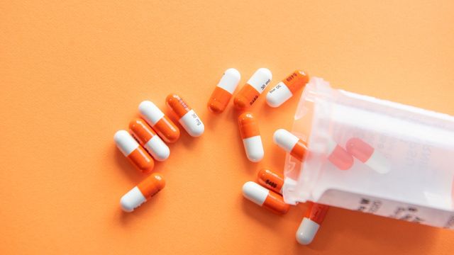 Orange and white pills spilling from a pill bottle. 