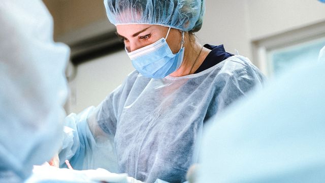 A female surgeon, wearing a hairnet, face mask and body covering operates on a patient. 