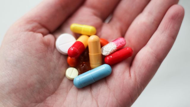 A hand holding pills and capsules of various shapes, sizes and colors. 