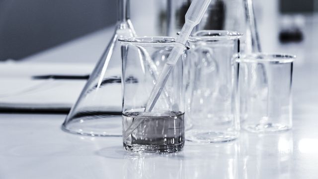 A collection of laboratory glassware on a white table, with a fluid-filled beaker in the center, also containing a pipette 