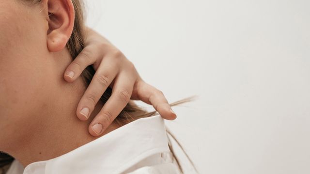 A woman holds the back of her neck.