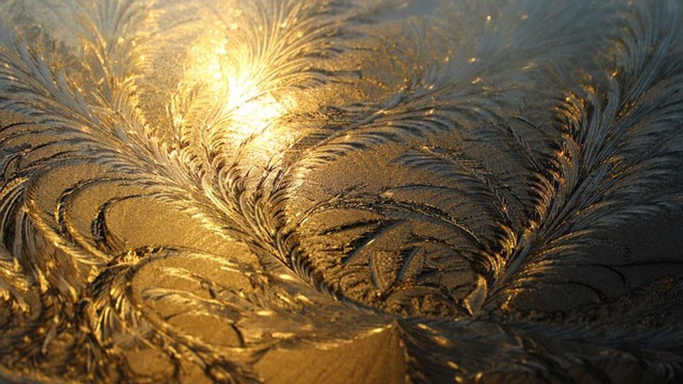 Photo showing the swirling, feathery patterns made by ice on a surface with light glinting off..