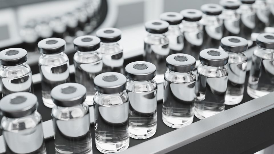 Clear glass vials filled with a colourless liquid sit on a conveyor belt.