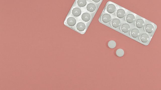 Two white blister packs lie on a pink surface next to two white tablets. 