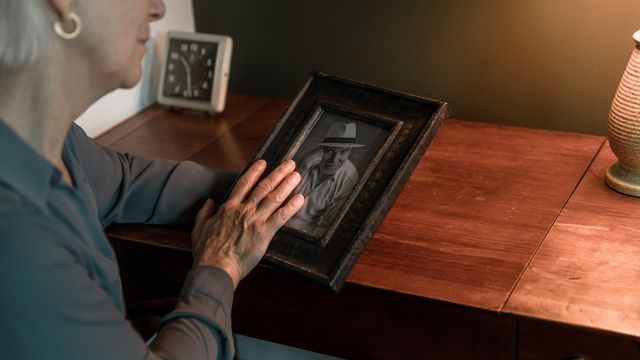 An older woman holds a framed greyscale image of a man.