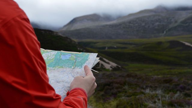 A person holding a map in front of a mountain.