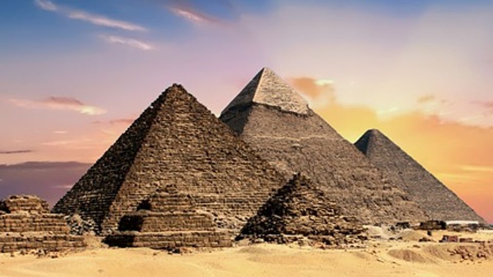 Group of large and small ancient Egyptian pyramids surrounded by sand.