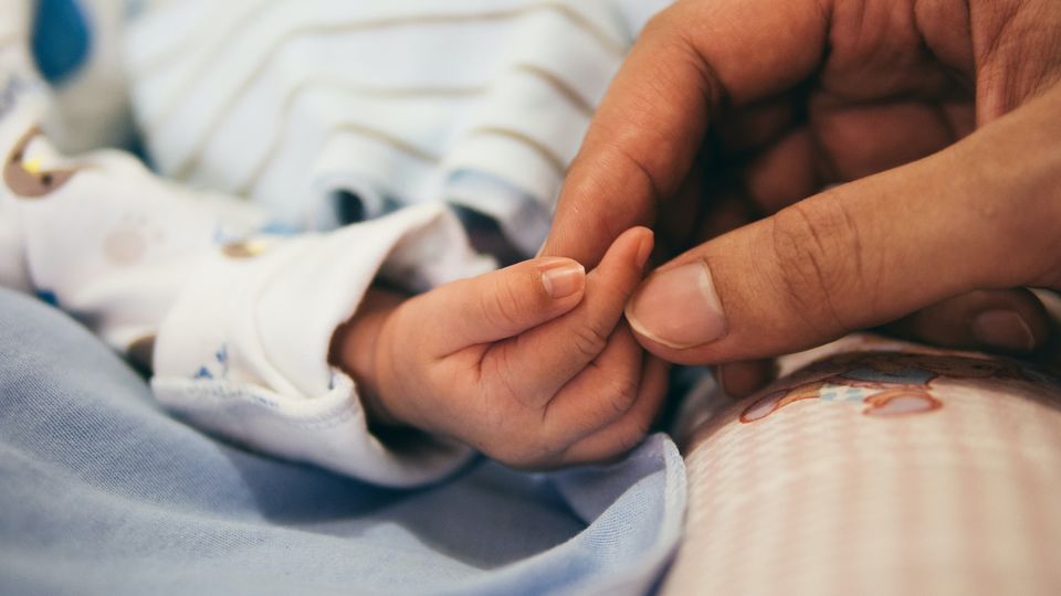 A parent holding a baby's hand.