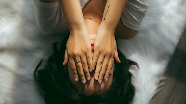 A woman holds her face while lying on a bed. 