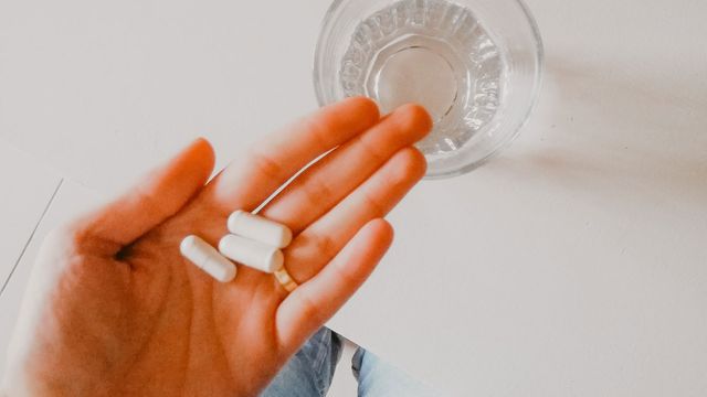 A person holding three white tablets with a glass of water in the background.
