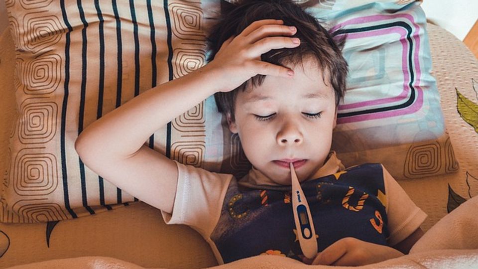 Boy in bed ill with flu, with a thermometer in his mouth.