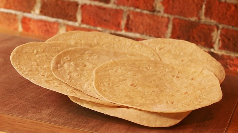 Stack of tortillas on a wooden table and a brick wall in the background.