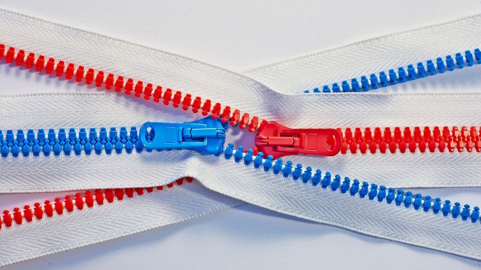 Two intertwined zips on a white background, one with red teeth and one with blue teeth.