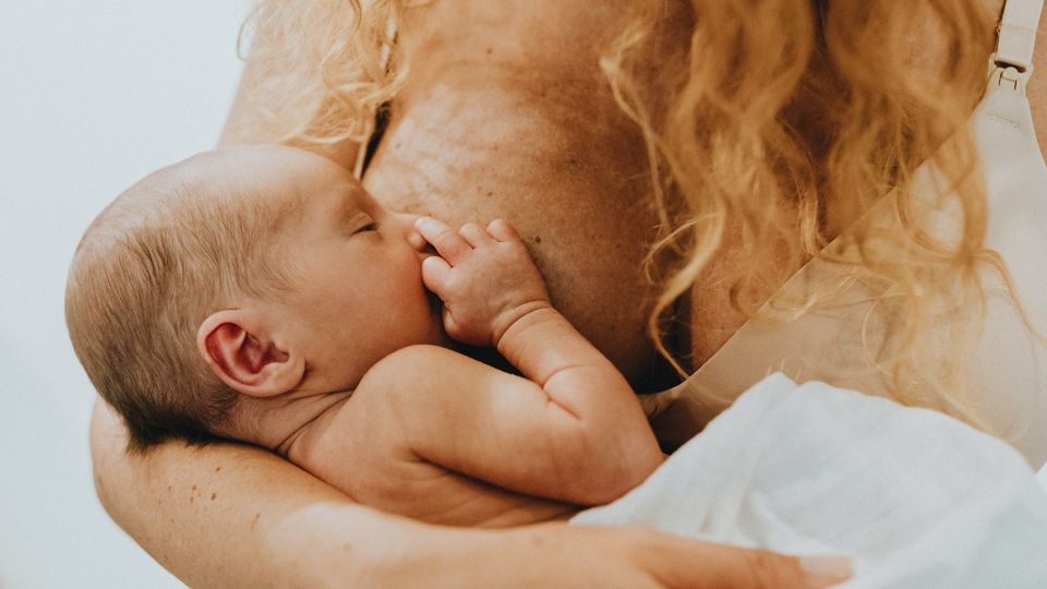 A baby held in the arms of a mother breastfeeds.