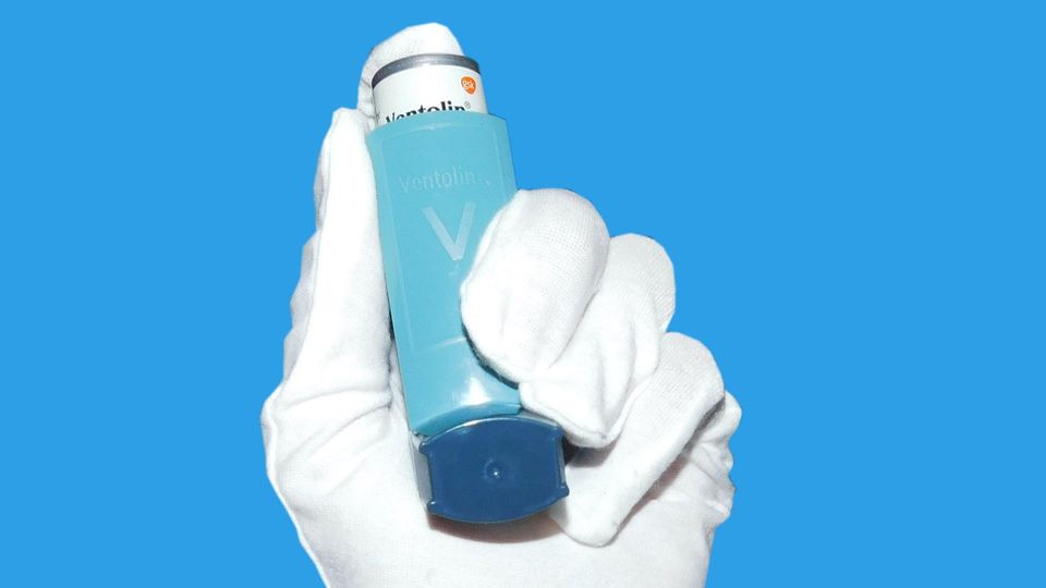 A gloved hand holding a blue inhaler.