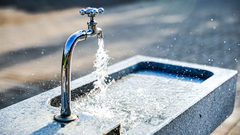 Outside sink with a tap, which is turned on and water is pouring out and splashing over the sink sides.