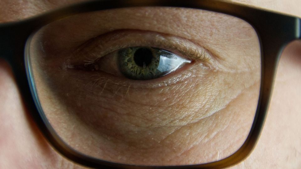 A closeup of a person's green eye through glasses lens.