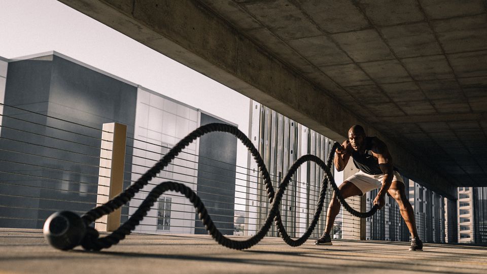 A man using battle ropes in a corcete parking garage. 