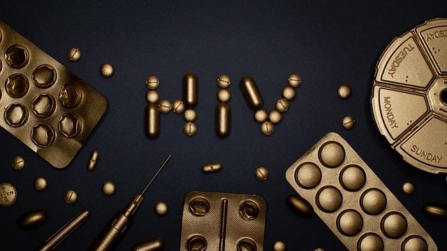 "HIV" spelled out in tablets sprayed gold surrounded by gold tablet packets and needles. 