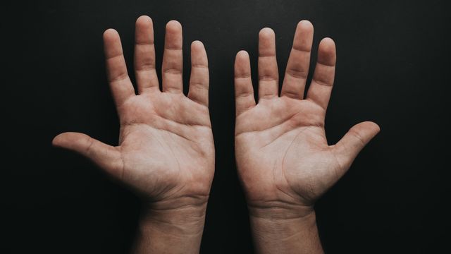 A pair of hands palms upward on a dark background. 