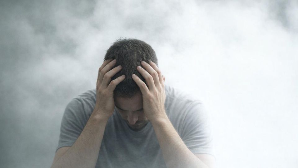 AI-generated image of a man holding his head in his hands surrounded by fog, representing brain fog.