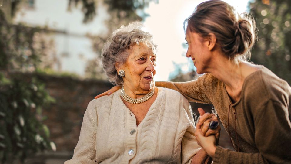An older woman greets a younger woman.