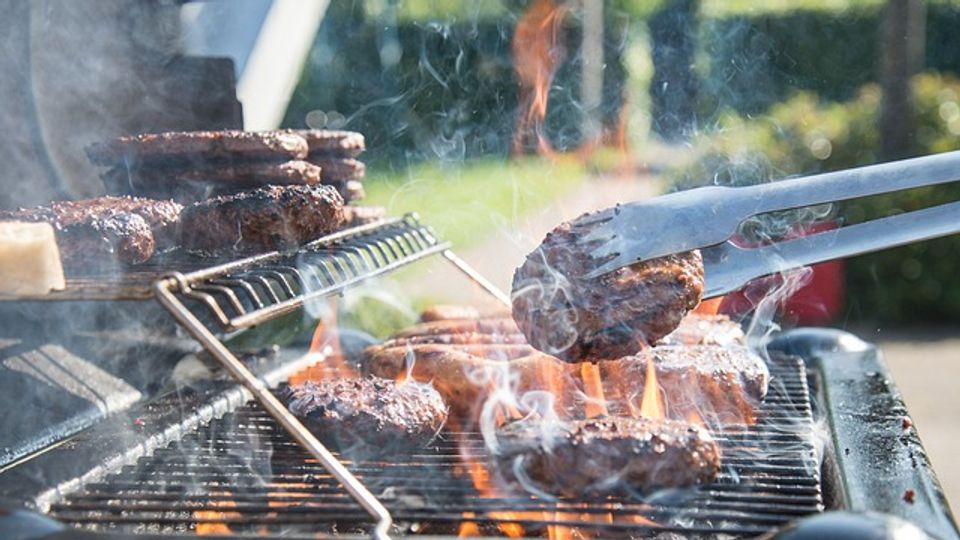 Barbeque with flames shooting up and metal tongs being used to turn meat-alternative burgers on the grill.