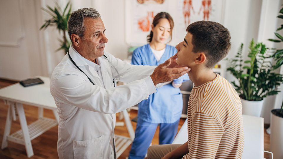 A doctor holds a patient's glands while a nurse takes notes.