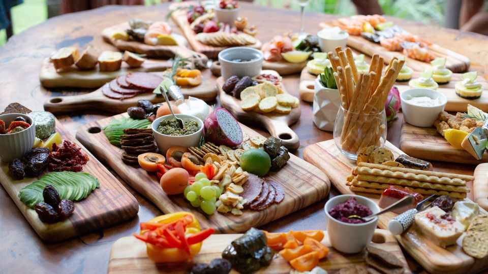 A selection of chopping boards, filled with meat, fruits, cheeses and breads.