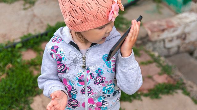 A toddler talking into a mobile phone. 