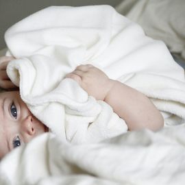Infant with bright eyes lying under a white blanket, symbolizing genetic health and care. 