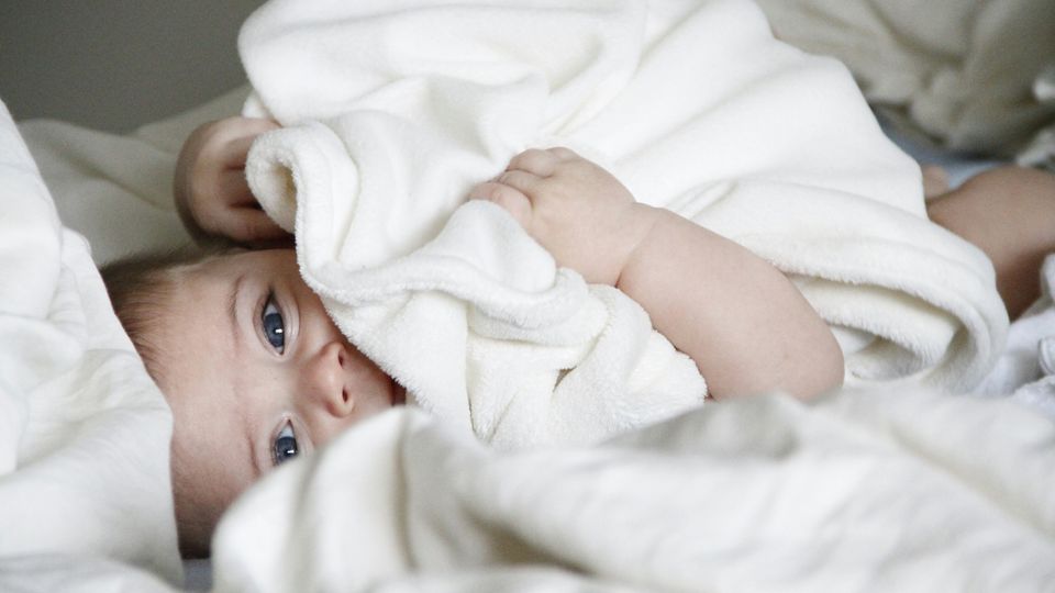 Infant with bright eyes lying under a white blanket, symbolizing genetic health and care.