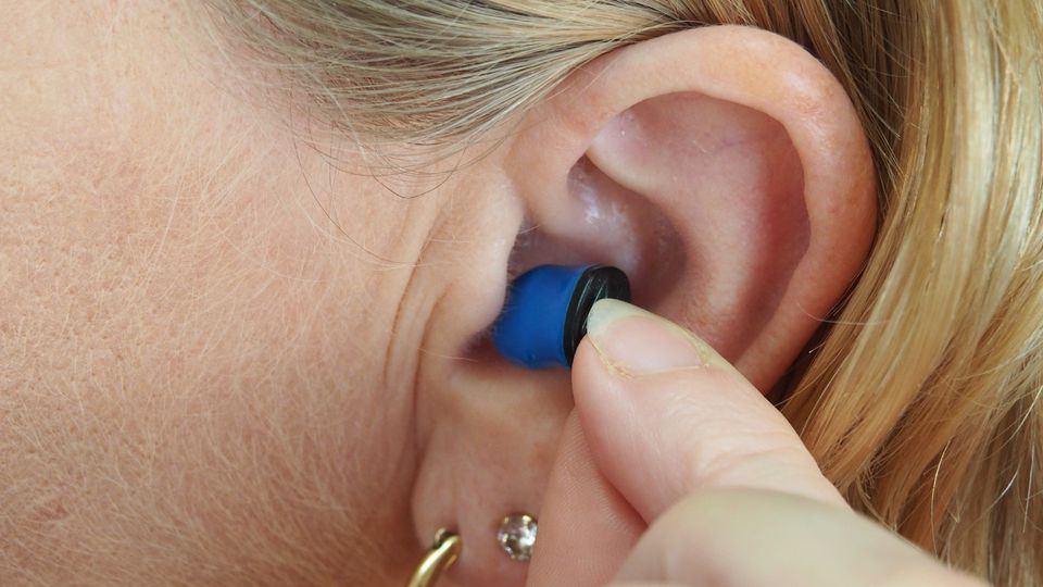 A woman puts a blue plug in her ear. 
